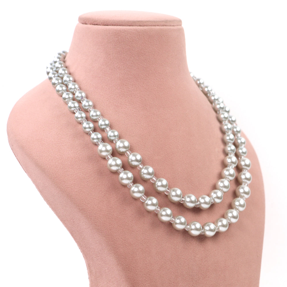 White double-strand glass pearl necklace with clear spacer beads and matching earrings on a pink display - Delemon Collection.