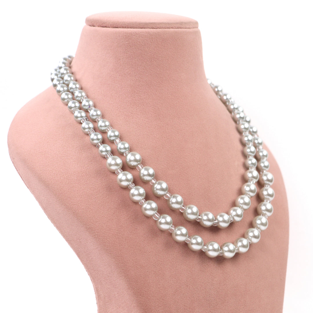 White double-strand glass pearl necklace with clear spacer beads and matching earrings on a pink display - Delemon Collection.